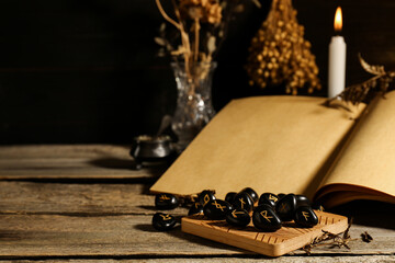Composition with black rune stones and old book on wooden table. Space for text