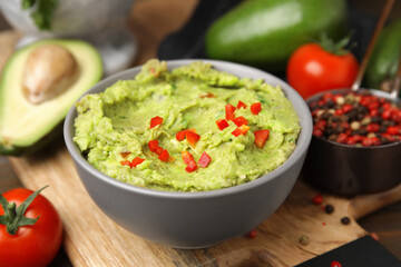 Bowl of delicious guacamole and ingredients on wooden board, closeup