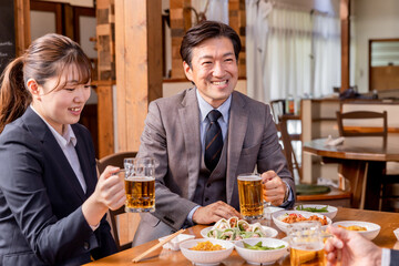 居酒屋で楽しい忘年会・新年会・飲み会・宴会をする仕事仲間・同僚・上司部下の男女
