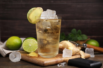 Glass of tasty ginger ale with ice cubes and ingredients on wooden table