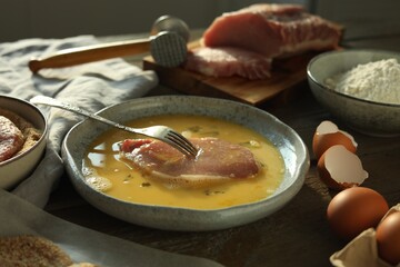 Cooking schnitzel. Raw pork chop in eggs, meat mallet and ingredients on wooden table