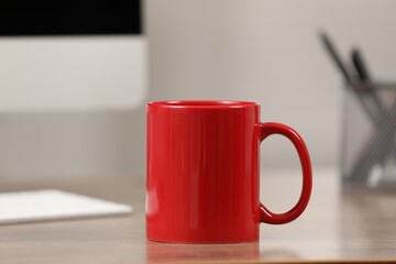Red ceramic mug on wooden table at workplace