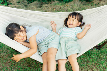 アウトドア・キャンプ場でハンモックに乗る子供・姉妹（外遊び）
