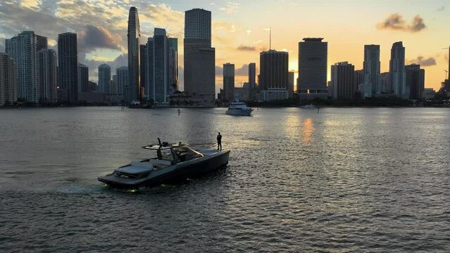 Aerial pull out wide shot of a man in a yacht near the Miami coastline and citiscape during sunset.