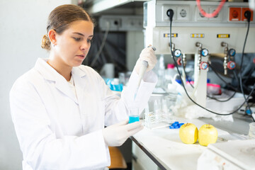 Smart young woman biologist in white coat using mechanical lab pipette for mixing chemicals in...