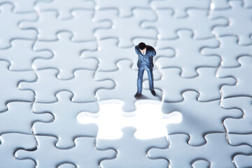 白いパズルと光る1ピースを覗き込むミニチュア人形