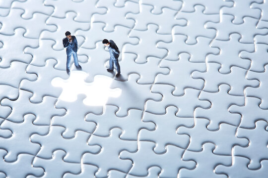 一面の白いパズルと光る1ピースを覗き込む2体のミニチュア人形
