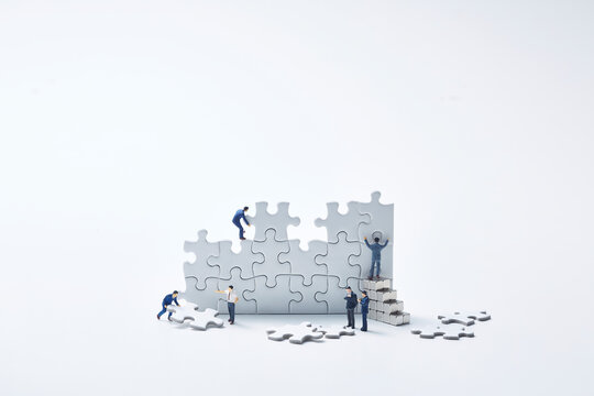白いパズルを組み立てる複数のミニチュア人形