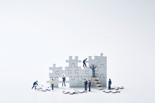 白いパズルを組み立てる複数のミニチュア人形