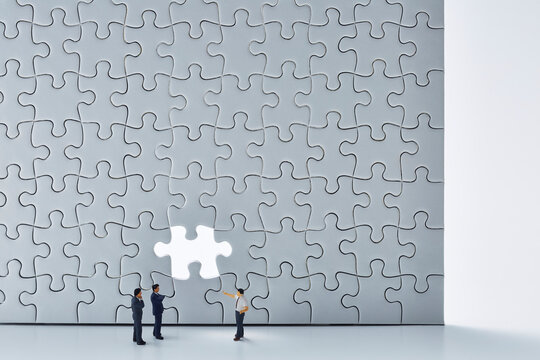 白いパズルの最後の空いた1ピースと3体のミニチュア人形