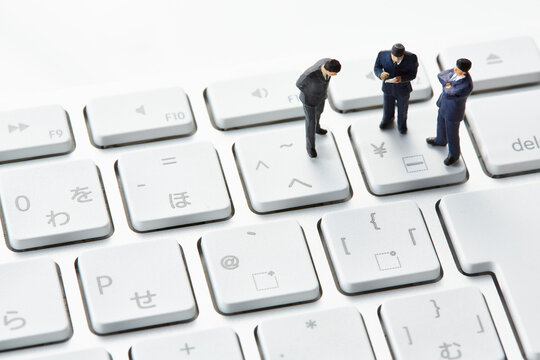 キーボードの上で考え事をする三体のミニチュア人形