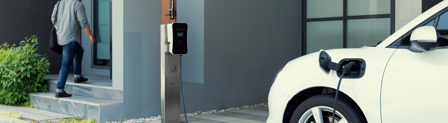 Progressive asian man and electric car with home charging station. Concept of the use of electric...