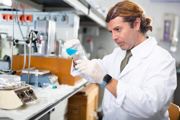 Focused male scientist chemist works with liquids in beaker in science laboratory
