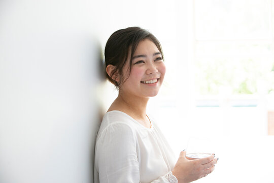 白い服を着て水の入ったグラスを持って笑っている女性