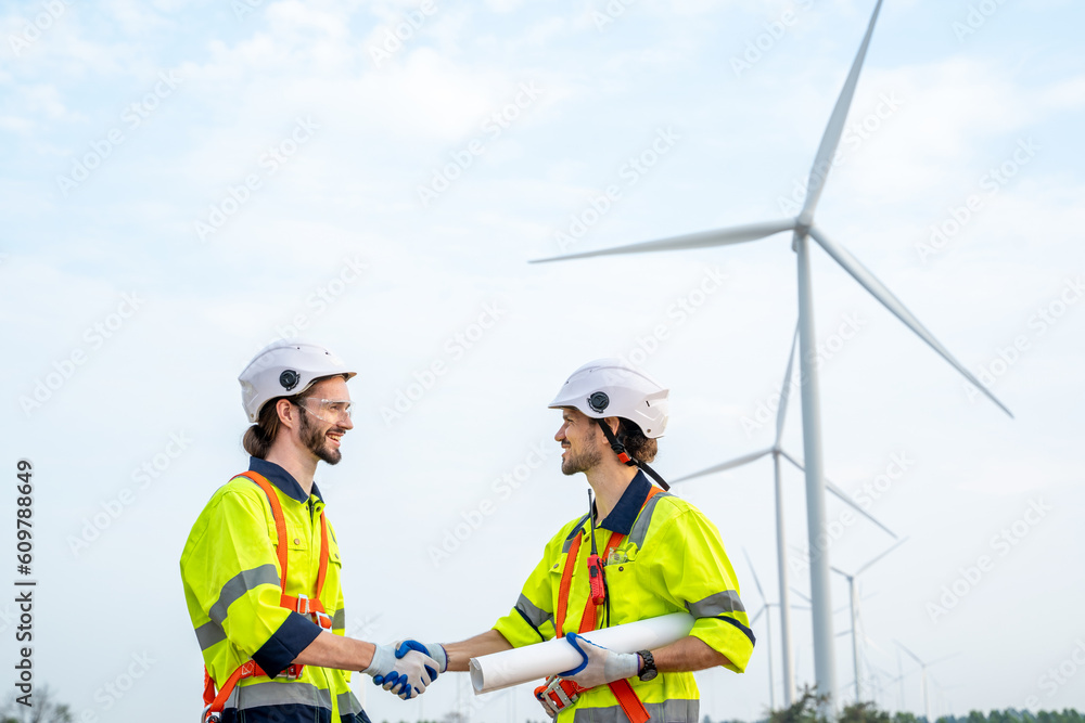 Poster engineers handshake after inspection work in wind turbine power generator station.