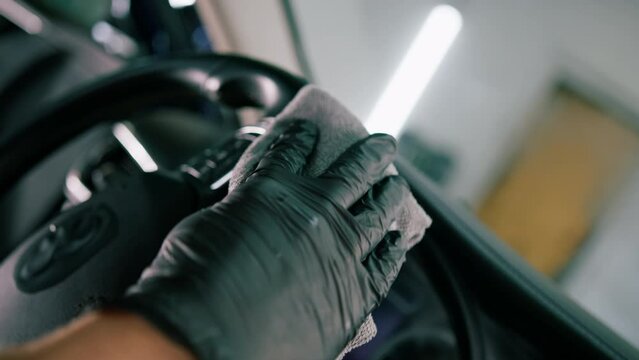 Detailing male car service employee performs dry cleaning and washing of car interior and steering wheel with a microfiber cloth close-up