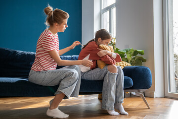 Caring mother cuddles teenage girl sitting on sofa and hug pillow. Concept mom care for child...