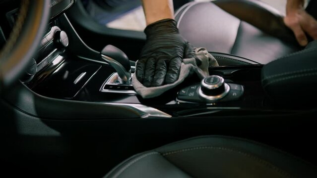 Detail of male car service worker performing dry cleaning and washing interior of a luxury car and gear selector with microfiber cloth
