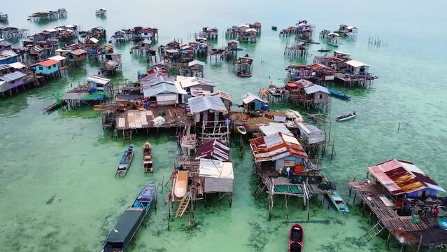 Drone flies sideways over water houses and boats of the Bajau Laut sea nomads with crystal clear sea water, at Pulau Omadal Semporna, Sabah, Malaysia.
