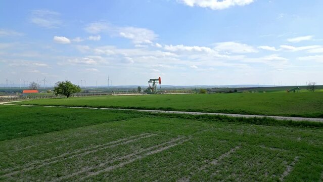 Drone Approach Towards Pump Jack Extracting Gas From Oil Field. Wind Farm In Distance. low aerial
