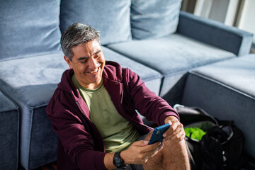 Fototapeta premium Middle aged latin man using a smart phone before going on a workout at home