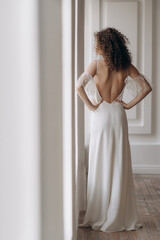 Beautiful lady stand by her back dressed in white long backless wedding dress with stylish elegance...