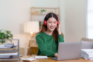 Cute Asian young woman wearing headphones using laptop computer at home. Asian woman using laptop, watching movie, listening to music, shopping online, watching live broadcast.