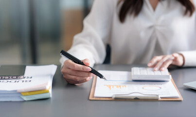 Close-up of businesswoman hands using a calculator to check company finances and earnings and budget. Business woman calculating monthly expenses, managing budget,  papers, loan documents, invoices.