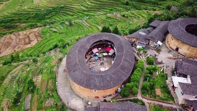 Orbiting aerial shot of the  Unesco World Heritage Tulou Hakka Houses on a mountain hill surrounded by green fields, Fujian China