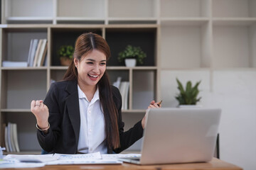 Beautiful Asian businesswoman celebrate while using laptop at office and showing delight. Startup small business and successful concept.