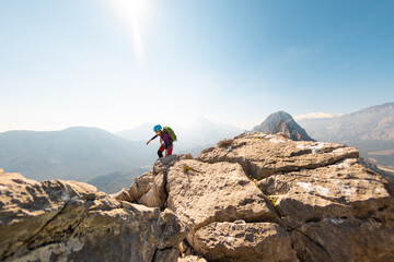young girl climber in a helmet and with a backpack walks along a mountain range against the...
