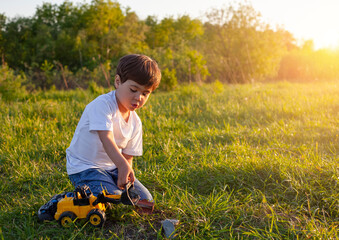 Cute little boy playing with toy car on green meadow at sunset