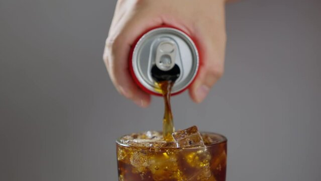A glass with ice being filled with carbonated soft drink, you can see the fresh bubbles of the beverage. Brown Soda Derives From The Red can pouring to a glass. Pouring Soda. Slow motion B roll 4k.