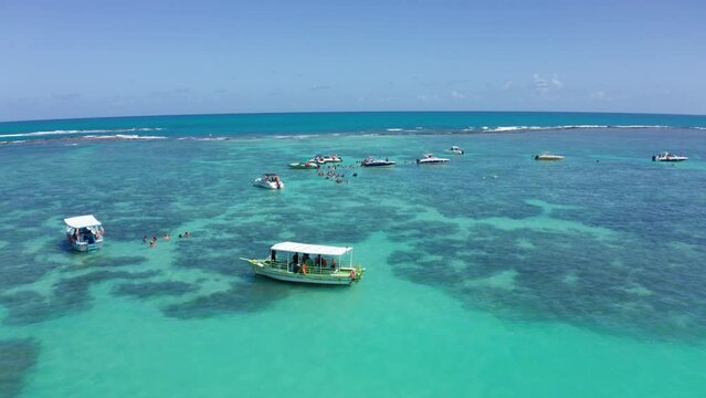 AERIAL - Tourist boats and people swimming in the turquoise waters of Maragogi, Brazil