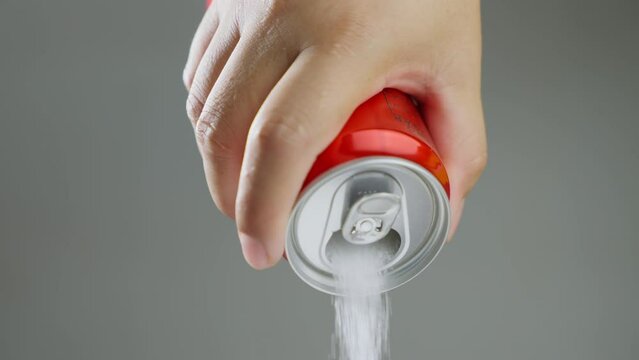 Unhealthy food - sugar in carbonated drinks. Red soda can pouring out white sugar showing an example of how bad and we all eat to much sugar. High amount of sugar in beverages. Slow motion.