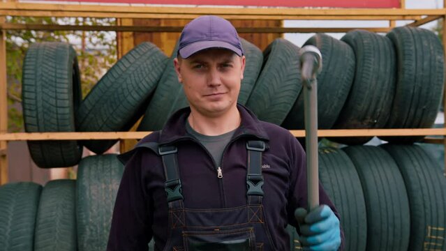 Portrait of a serious man Auto mechanic showing Thumb signal with a cylinder wrench in his hand on the background of car tires detailing auto repair
