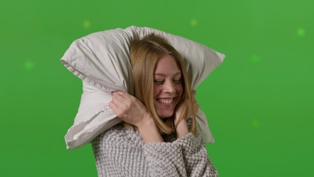 Young caucasian woman holding white pillow over green color background wall. People emotion lifestyle concept. Beautiful slim girl dancing and having fun