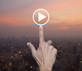 Hand pressing play button flat icon over blur of cityscape on warm light sundown, Business music...