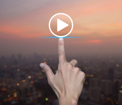 Hand pressing play button flat icon over blur of cityscape on warm light sundown, Business music online concept