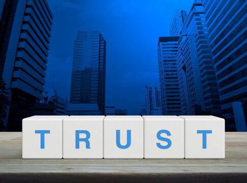 Trust letter on white block cubes on wooden table over modern office city tower and skyscraper, Building trust business concept