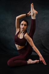 Fototapeta na wymiar Attractive caucasian slim woman in sport cloth doing yoga stretching at studio black background