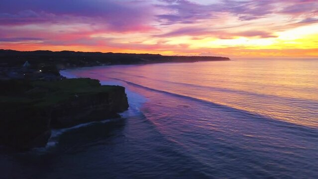 Indo vibrant orange red purple pink sunset sunrise view of surf coastline cliffside resort aerial drone cinematic Padang Bali Kuta Uluwatu beach Indonesia town city Lombok circling right movement