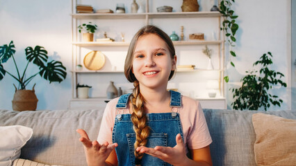 Influencer kid. Video presentation. Internet call. Confident smiling blogger girl talking gesticulating with hands on sofa in cozy room at home.