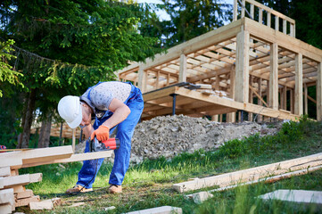 Carpenter using circular saw for cutting wooden plank. Man worker building wooden frame house. The ideology behind modern, environmentally-conscious construction.