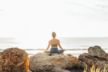 Woman meditating on rock at beach in front of sky