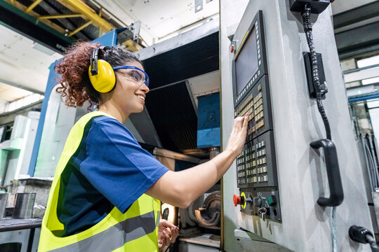 Maintenance engineer in protective workwear operating CNC machine in factory