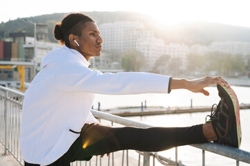 Athlete with wireless in-ear headphones stretching near railing
