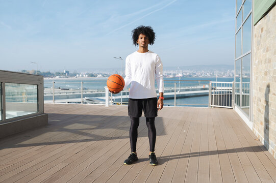 Young athlete with basketball standing on pier at sunny day