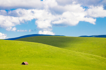 Idyllic landscape with an old cottage at the foot of some hills with green grass. Perfect for wallpaper or decorative