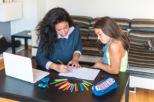 Freelancer mother guiding daughter drawing in notebook with laptop on table